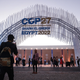 Attendees photograph one another outside the main entrance of the COP27 conference. They're standing under a large arch made of white.